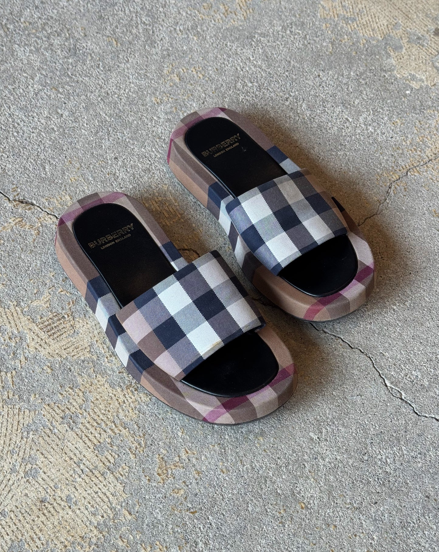 Plaid burberry patterned slides on a concrete floor
