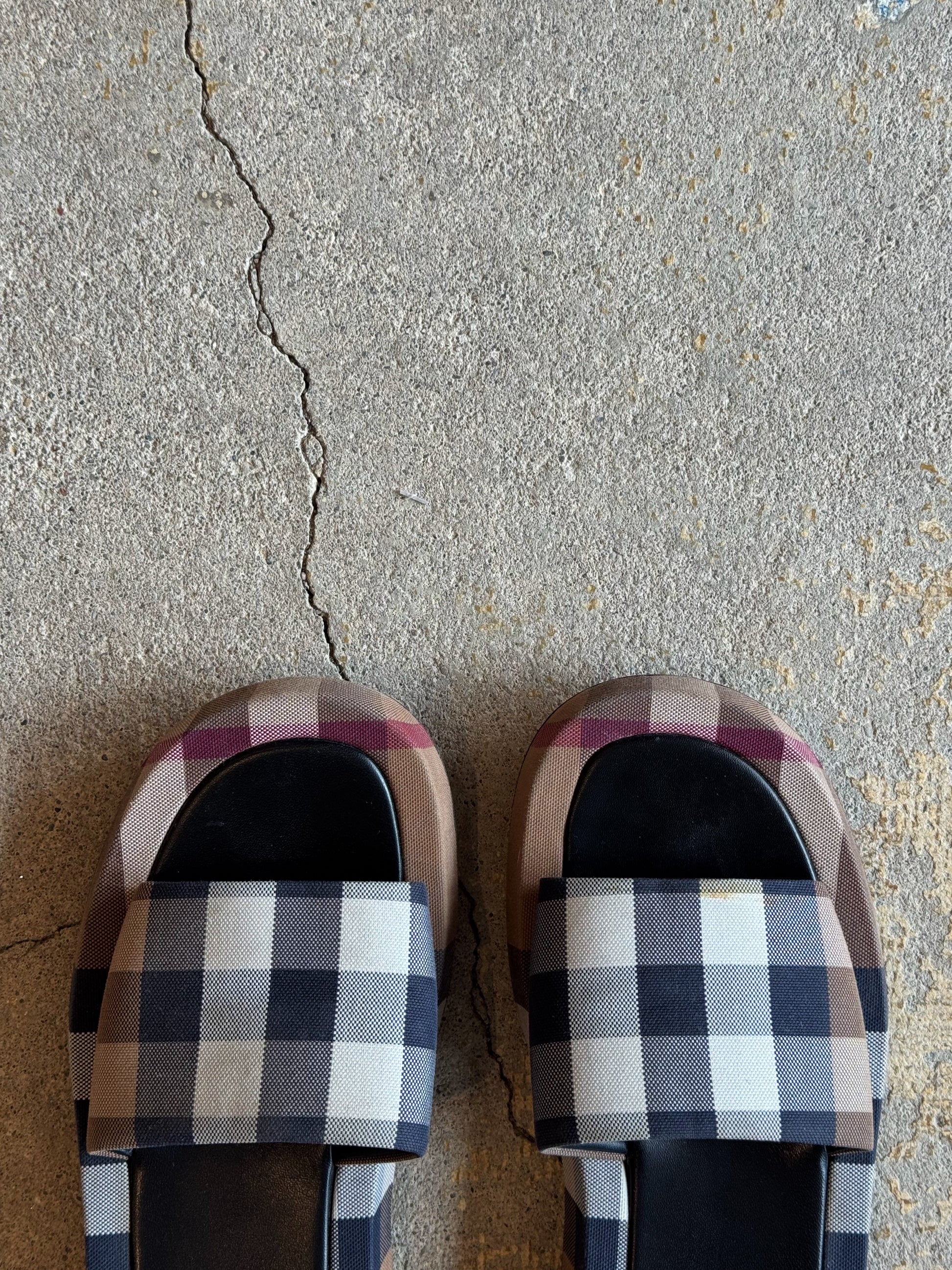 Plaid burberry patterned slides on a concrete floor