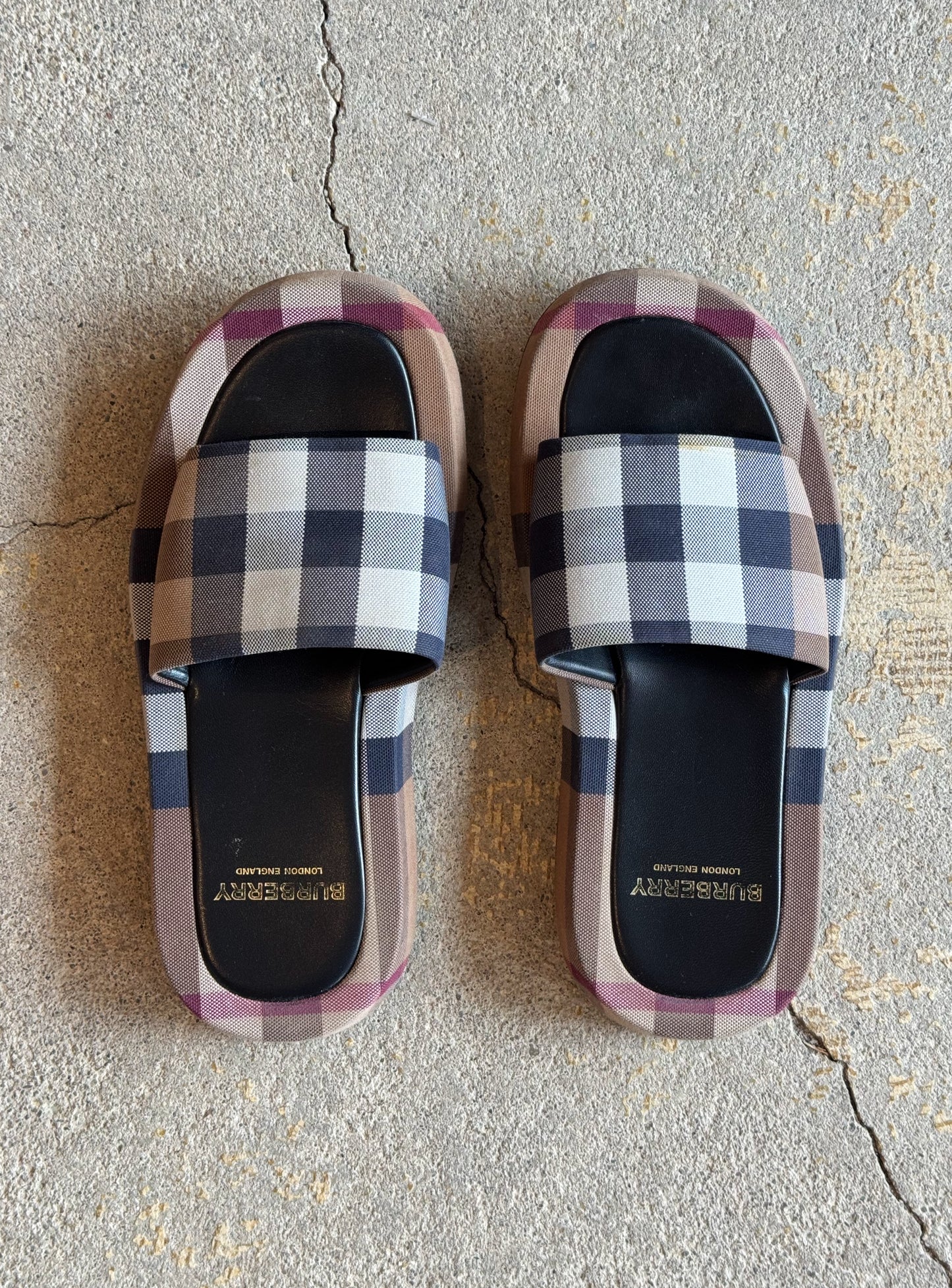 Plaid burberry patterned slides on a concrete floor