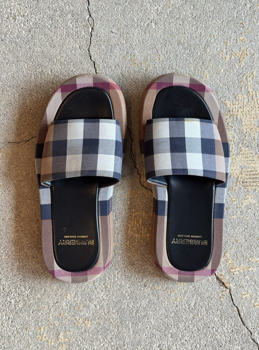 Plaid burberry patterned slides on a concrete floor