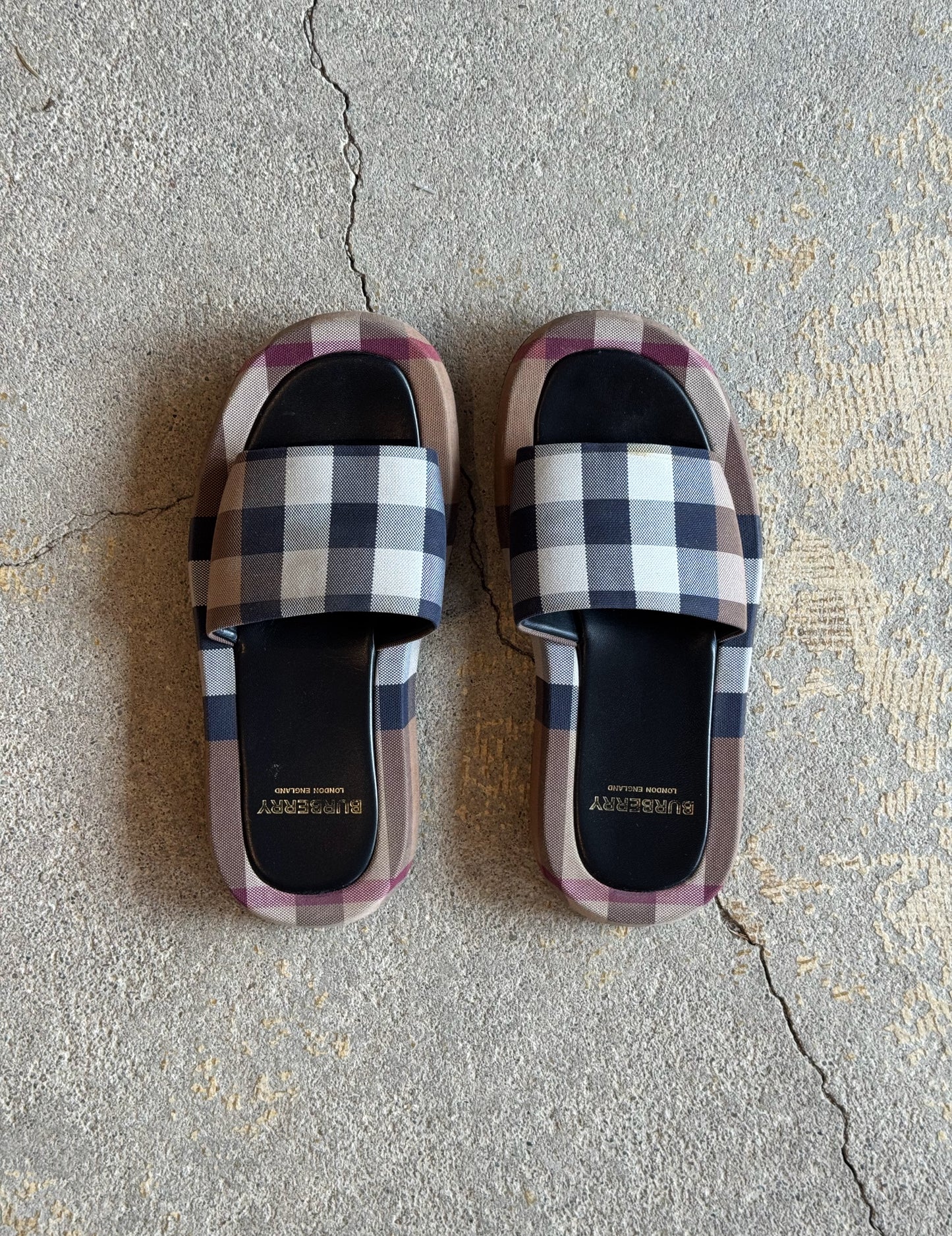 Plaid burberry patterned slides on a concrete floor