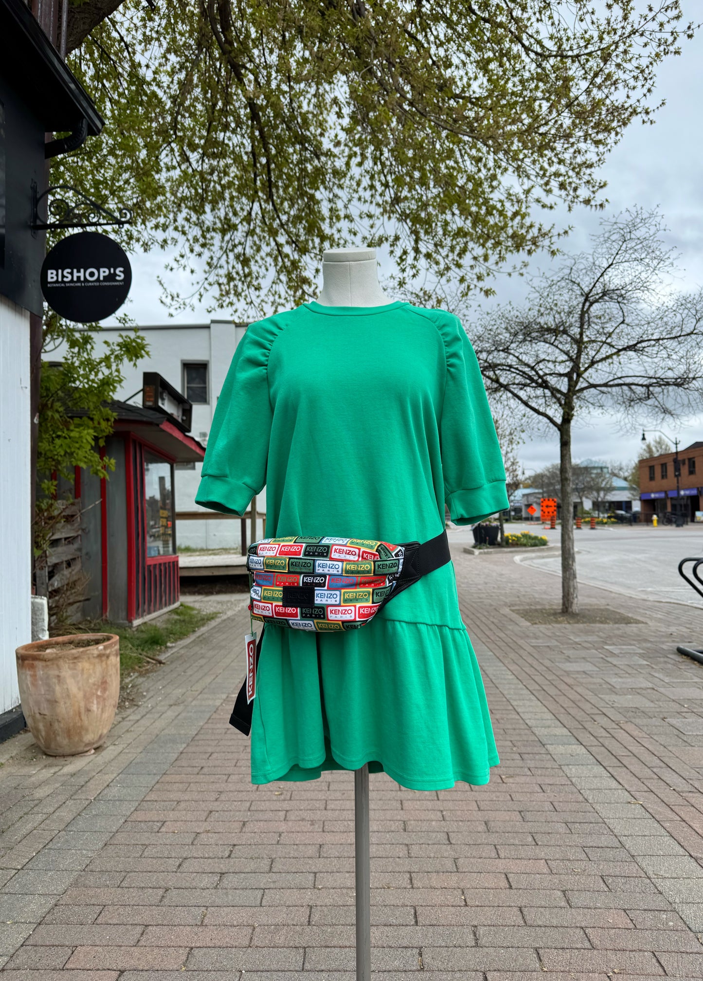 Green dress on a mannequin with a colourful Kenzo fanny pack in an outdoor setting.