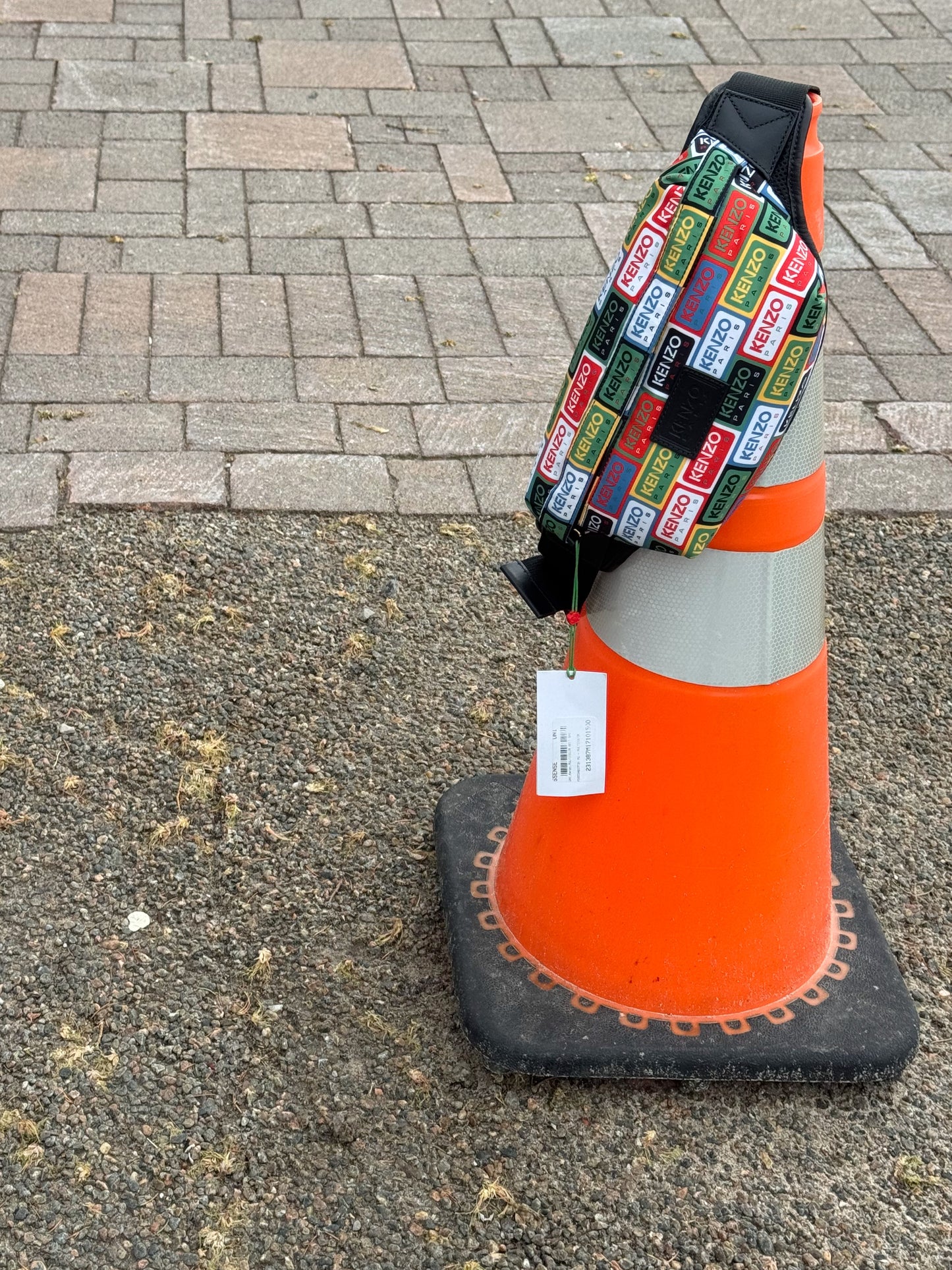 Orange traffic cone with a colorful patterned Kenzo Crossbody on top in an outdoor setting.
