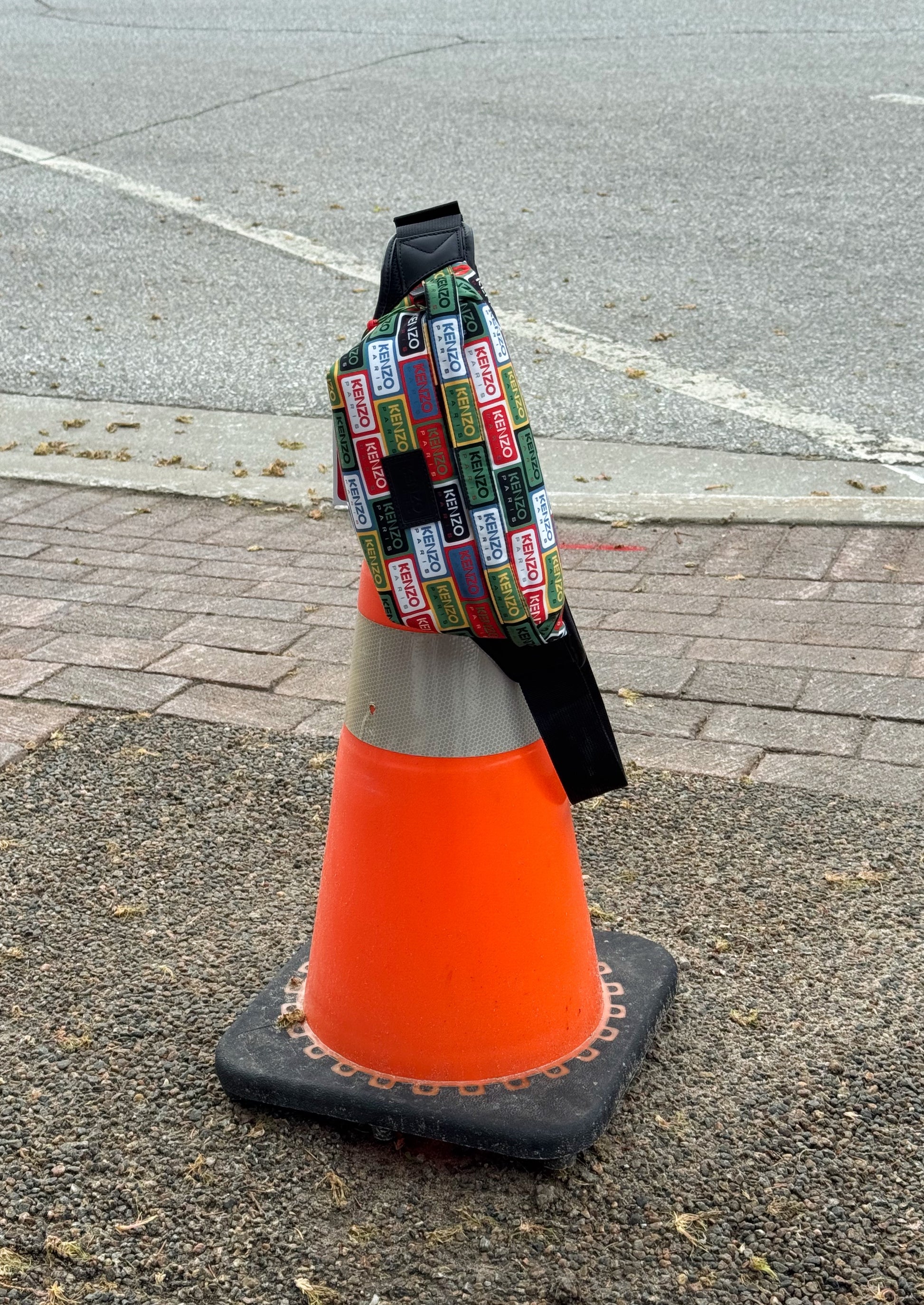 Orange traffic cone with a colorful patterned Kenzo Crossbody on top in an outdoor setting.