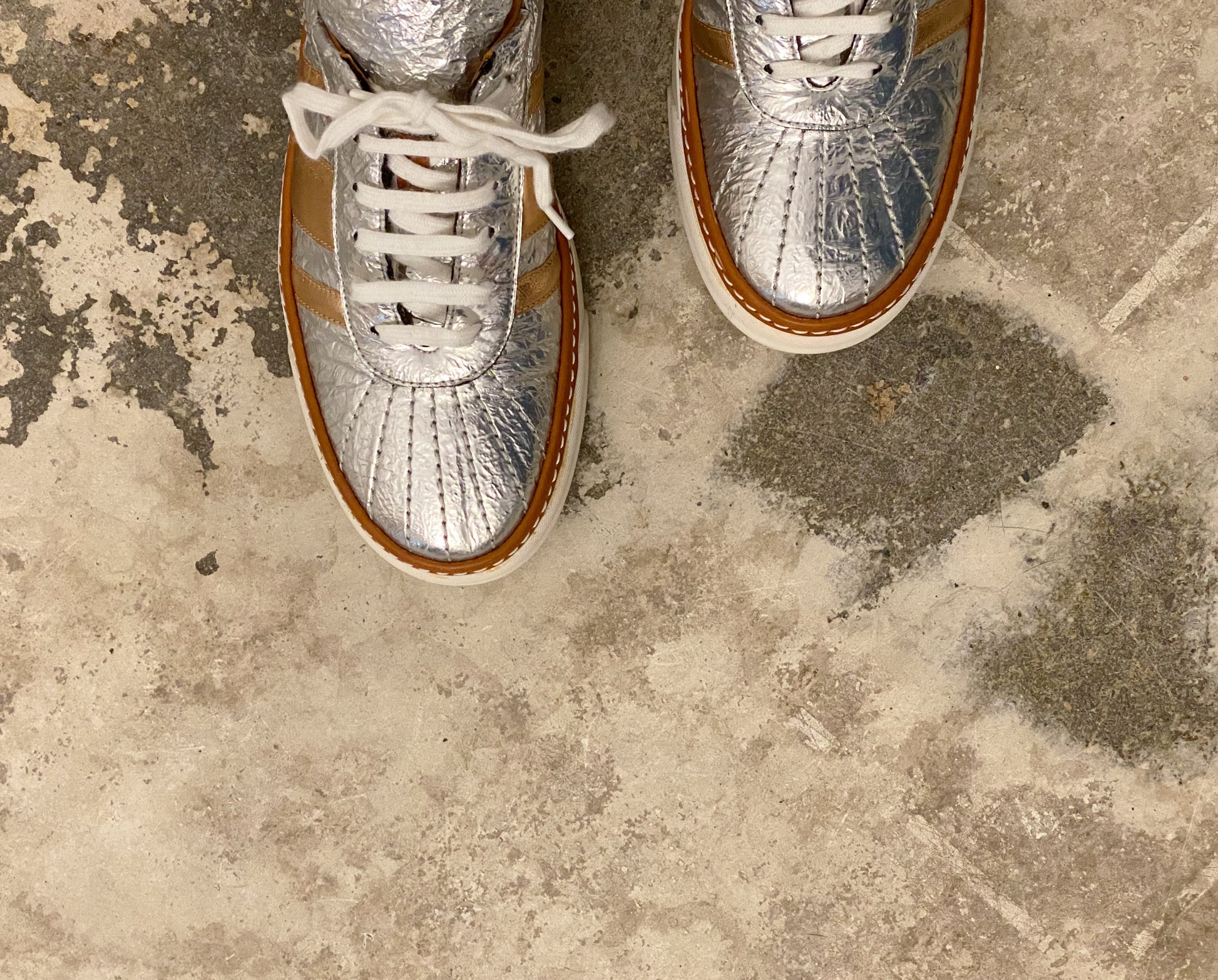 Silver sneakers with brown soles on a concrete floor. M by Missoni silver & bronze lamé low top sneakers