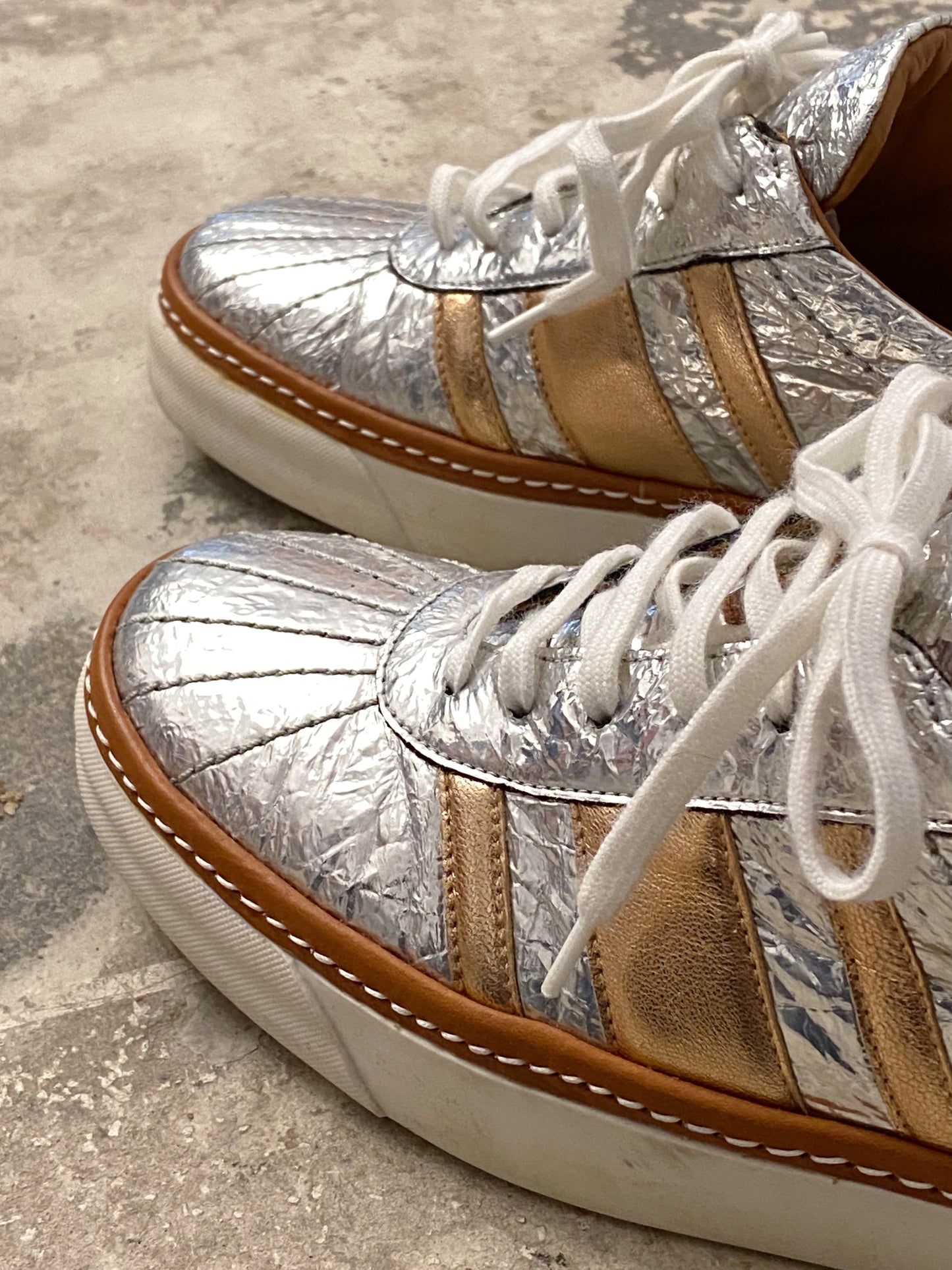 Silver sneakers with white laces on a concrete surface. M by Missoni silver & bronze lamé low top sneakers