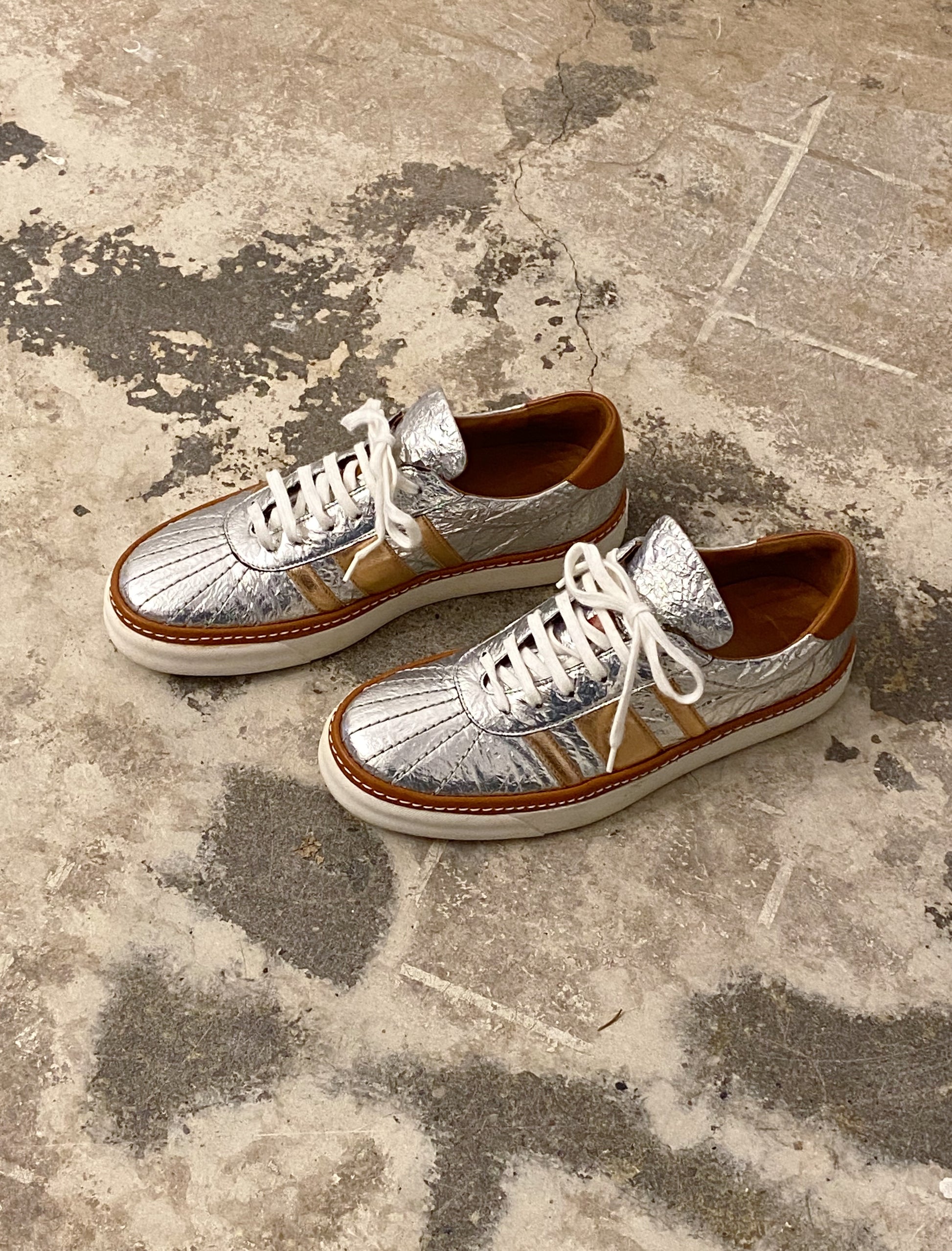 Pair of silver and gold sneakers on a textured concrete floor