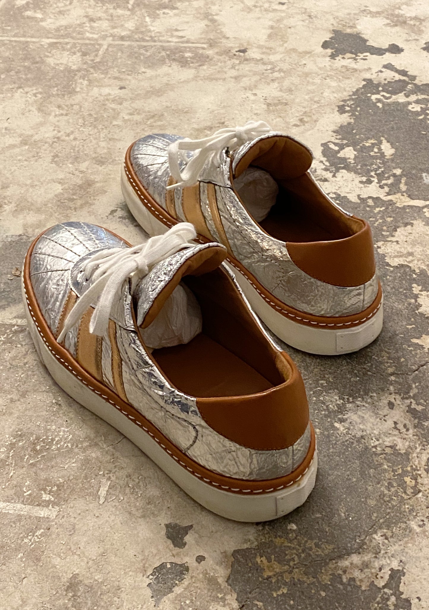 Pair of metallic and brown sneakers on a textured concrete floor. M by Missoni silver & bronze lamé low top sneakers