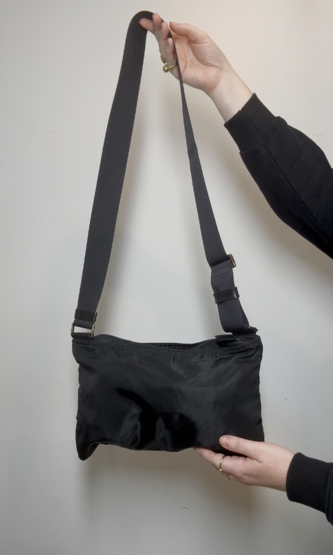 Black Prada crossbody bag with a strap held by a person against a plain background