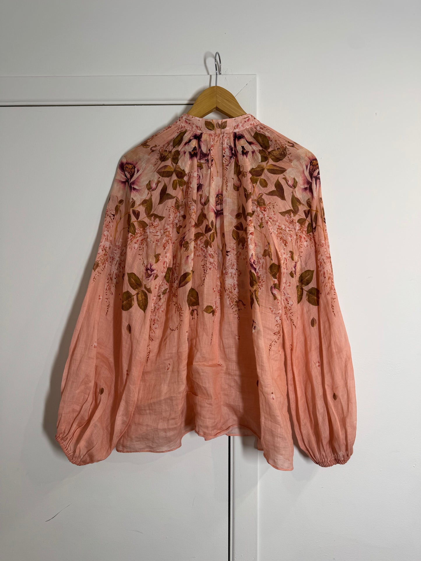 Pink floral Zimmermann blouse on a hanger against a white wall