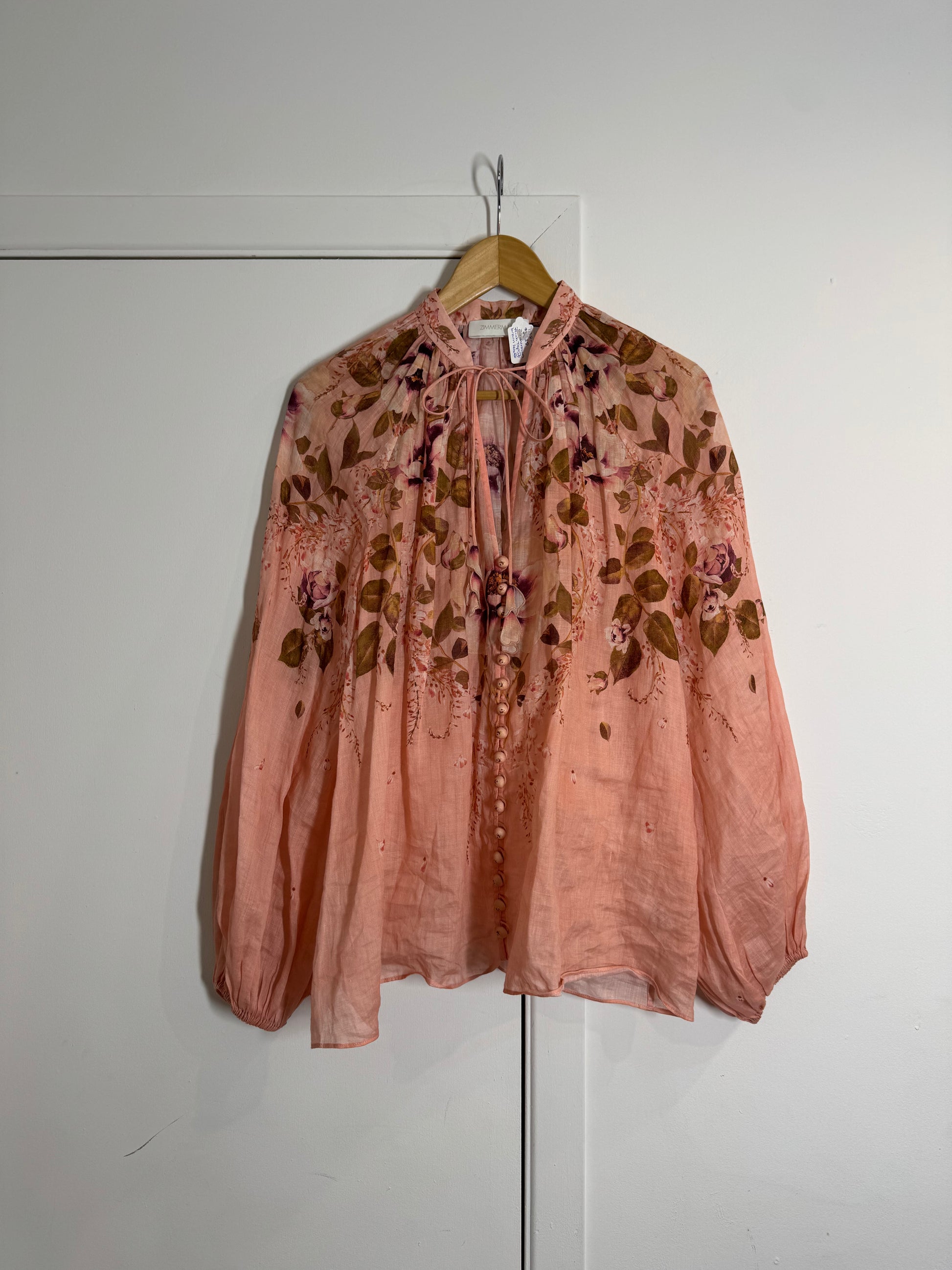 Pink floral Zimmermann blouse on a hanger against a white wall