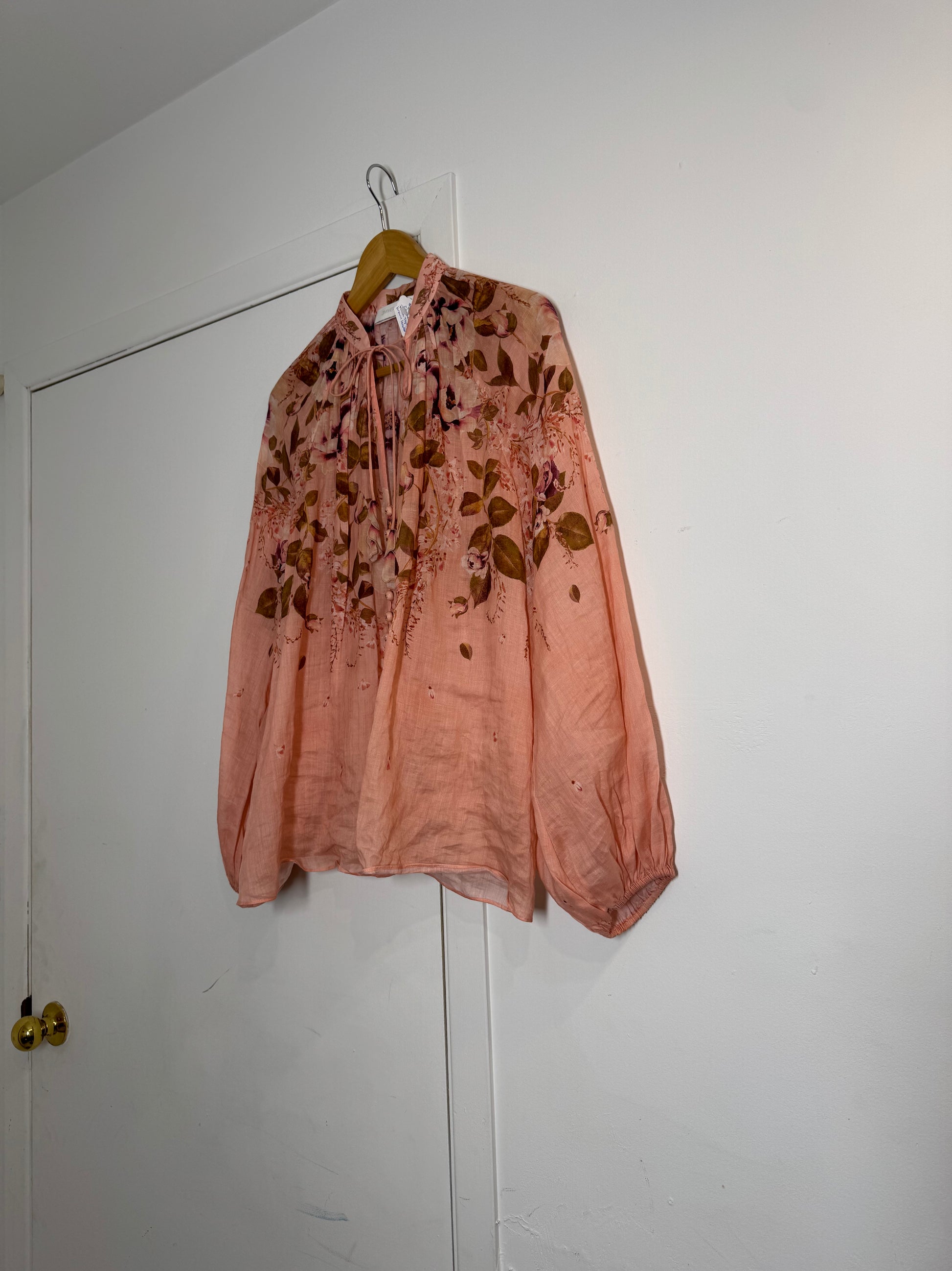 Pink floral Zimmermann blouse hanging on a hook against a white wall.